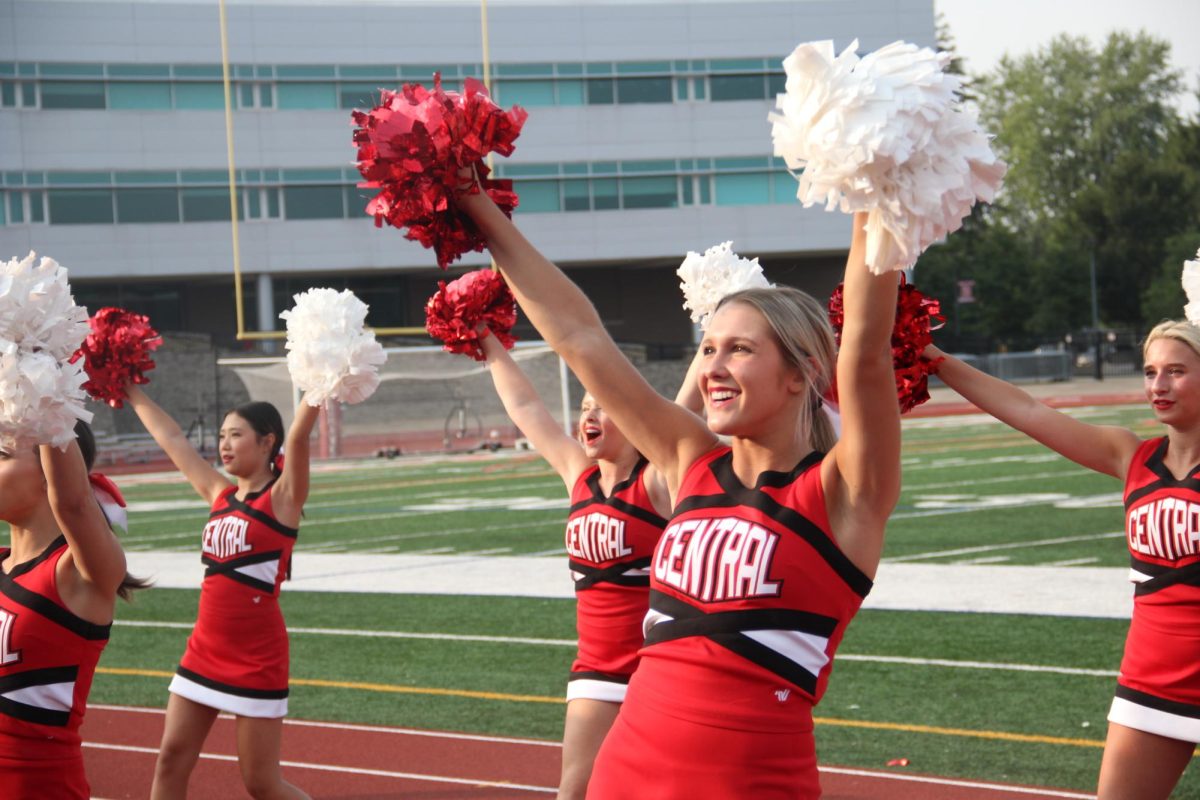 Cheer team member and junior Claire Poulaki waves to the student section during varsity football's scrimage at Central's Red and White Night.