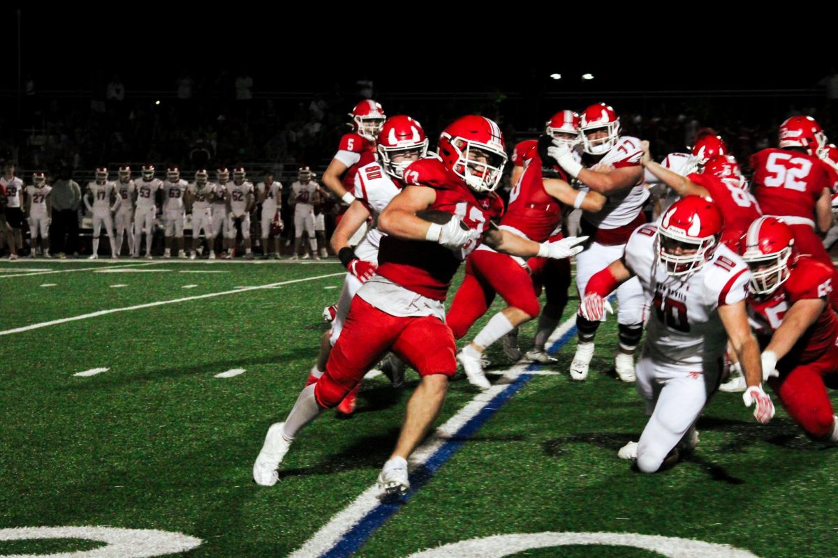 Running back Aiden Clark (13), a senior, sprints through defenders on Aug. 30. Clark would go on to score two touchdowns, helping the Redhawks in a 24-13 victory against Hinsdale Central.